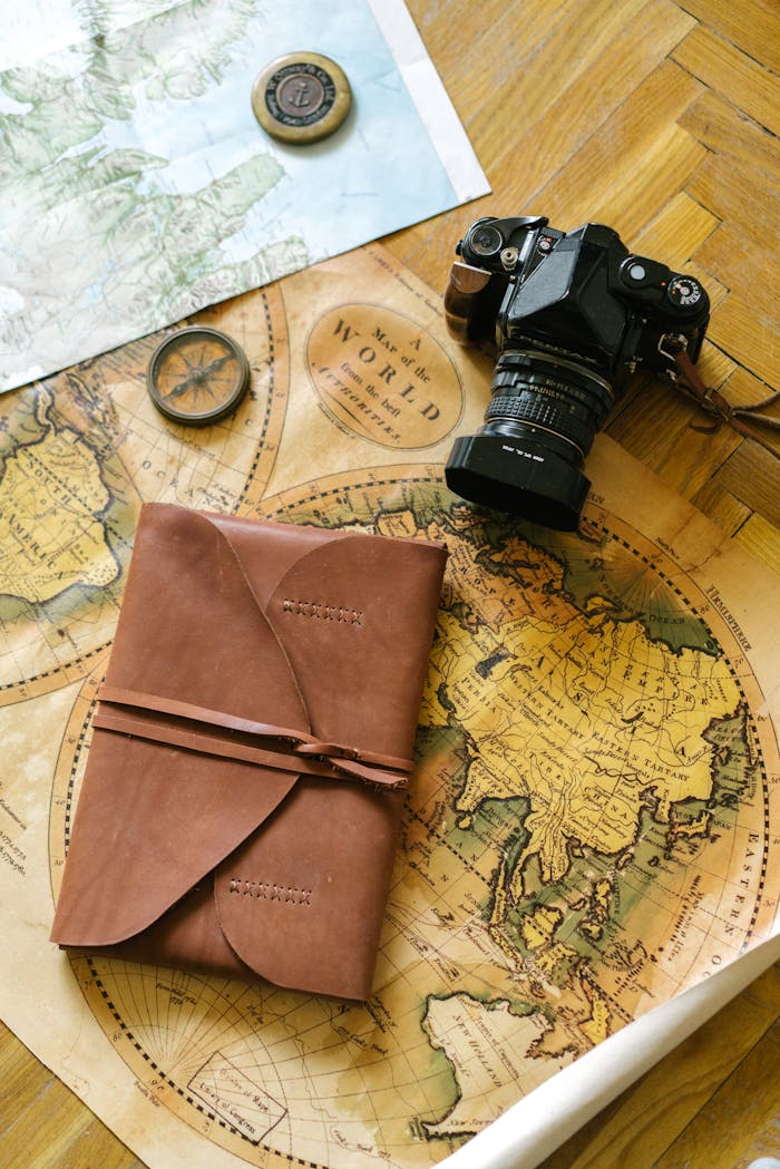 Flat lay of vintage travel items including a map, camera, and leather journal, perfect for wanderlust inspiration.