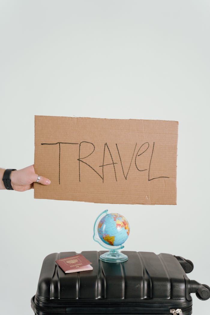 Creative travel concept featuring a cardboard sign, globe, passport, and suitcase against a white background.