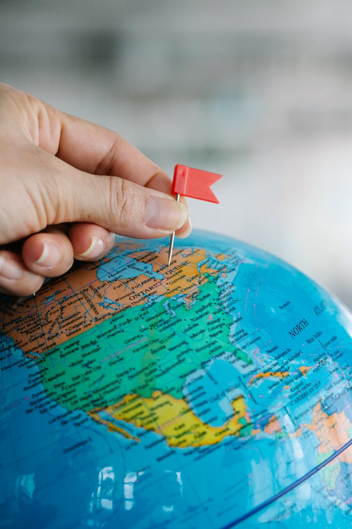 Close-up of a hand placing a red flag pin on the North America region of a globe.